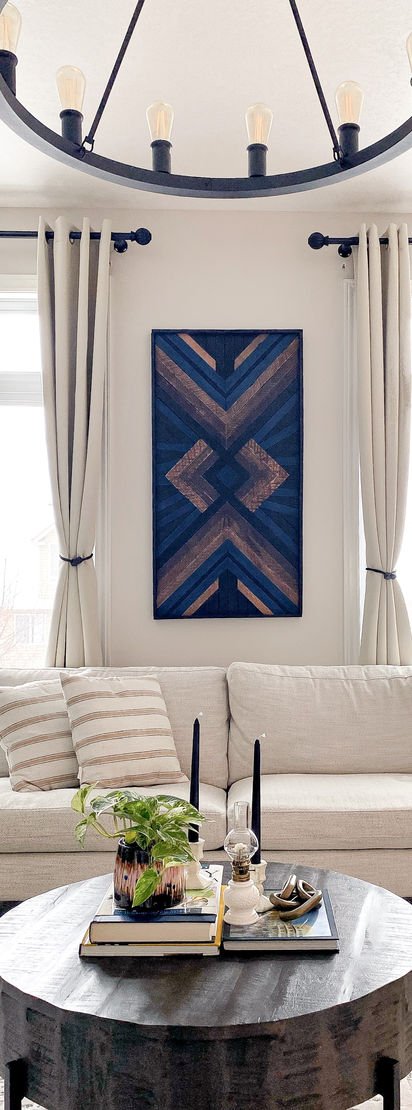 A navy and copper geometric wood panel above a cream sofa, under a black iron chandelier.