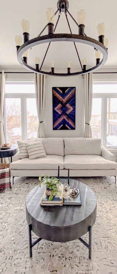 A black orb chandelier over a cream sofa, with the navy and copper geometric panel between the curtains and a round grey coffee table.