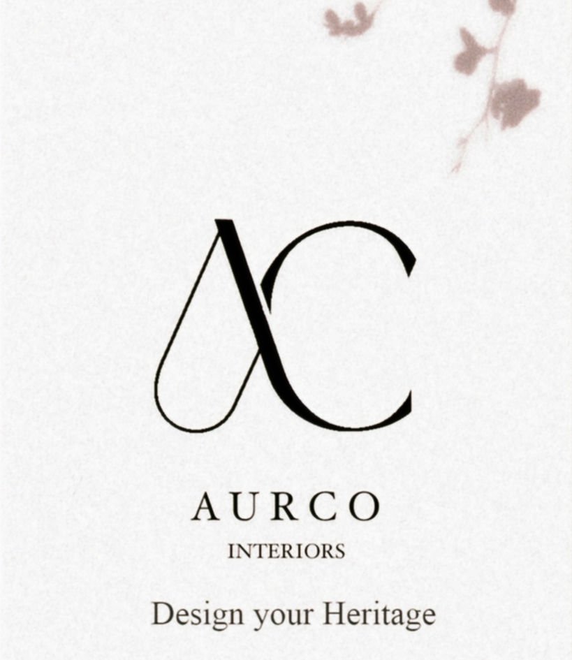 The AURCO mark printed on paper: an A and a C drawn over one another sharing a single stroke, with AURCO INTERIORS and Design your Heritage set beneath, and the shadow of a dried branch across the corner.